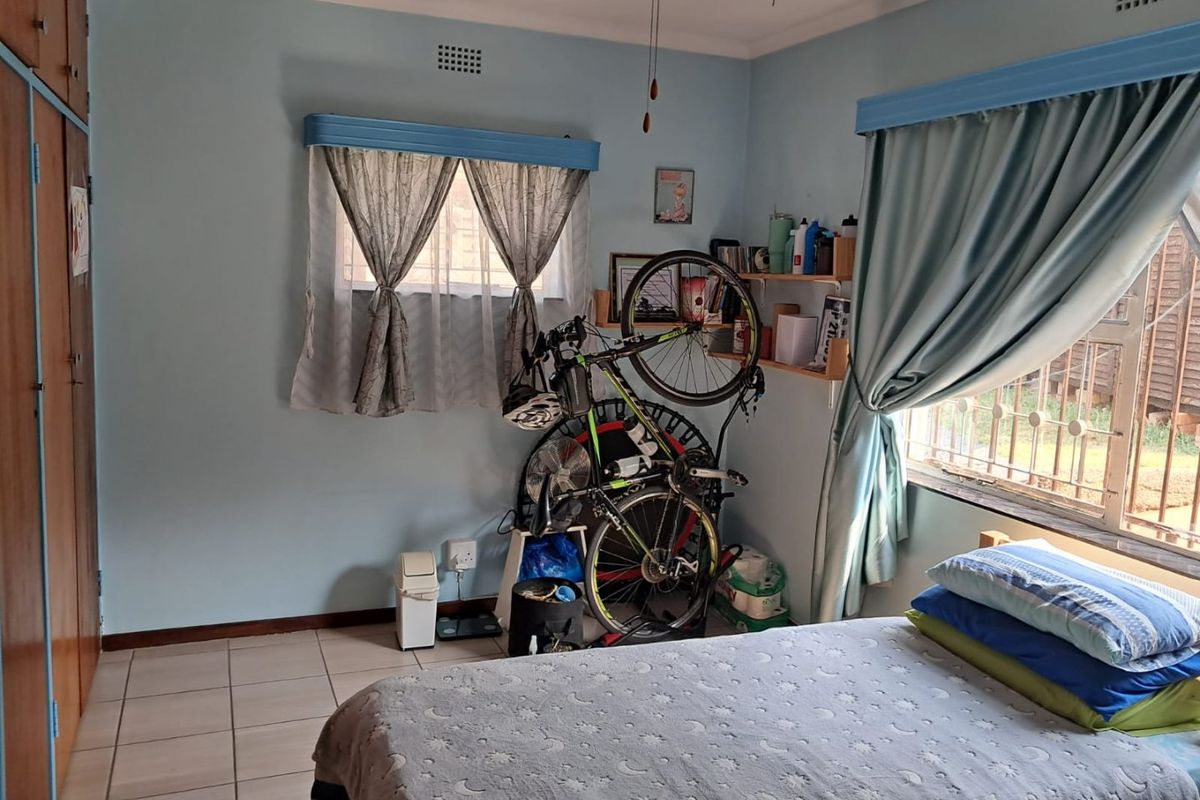 A functional bedroom featuring built-in cupboards, tiled flooring, and security burglar bars on the windows.