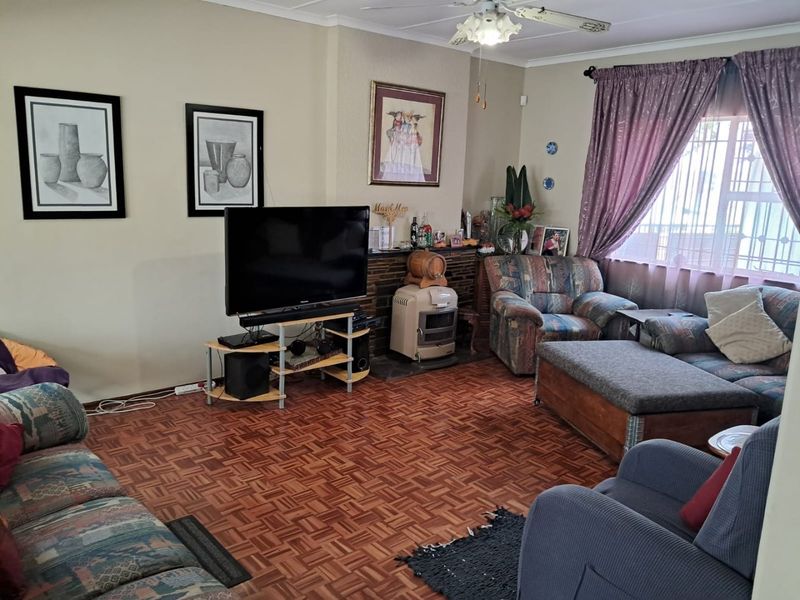 A living room featuring traditional parquet flooring, a brick fireplace, and a ceiling fan, offering a classic layout with natural light.