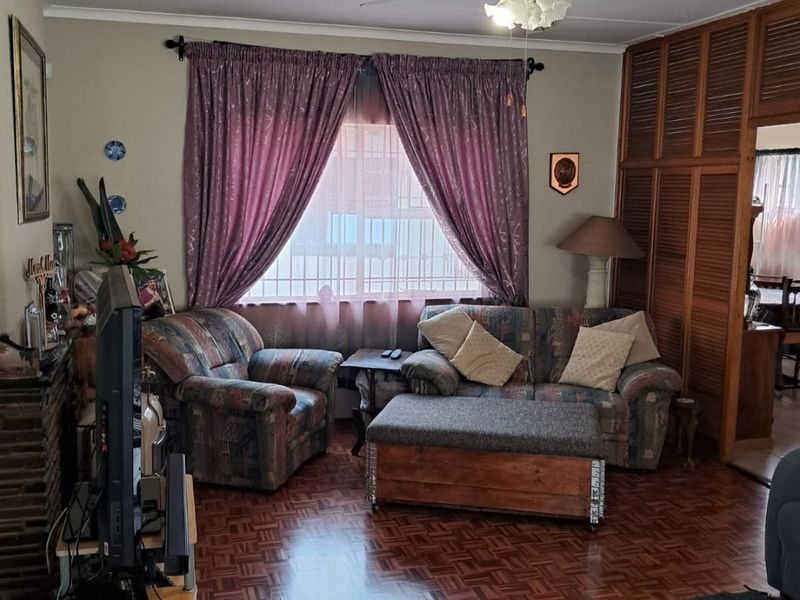 A cozy living room featuring classic parquet flooring, a ceiling fan, and a built-in wooden room divider, offering a traditional and functional layout.