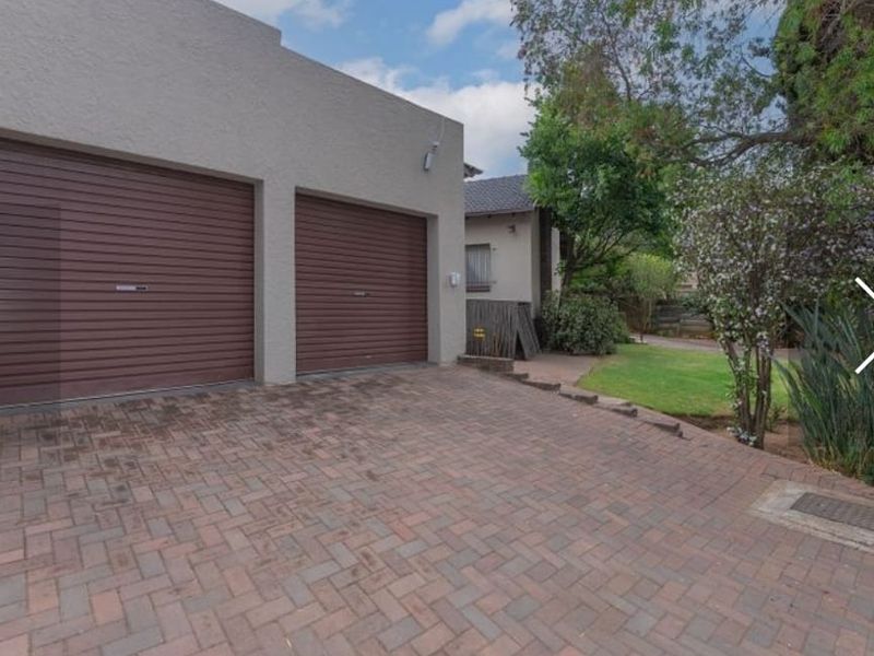 A well-maintained front exterior featuring a double garage with roller shutter doors and a paved driveway leading to a landscaped garden area.