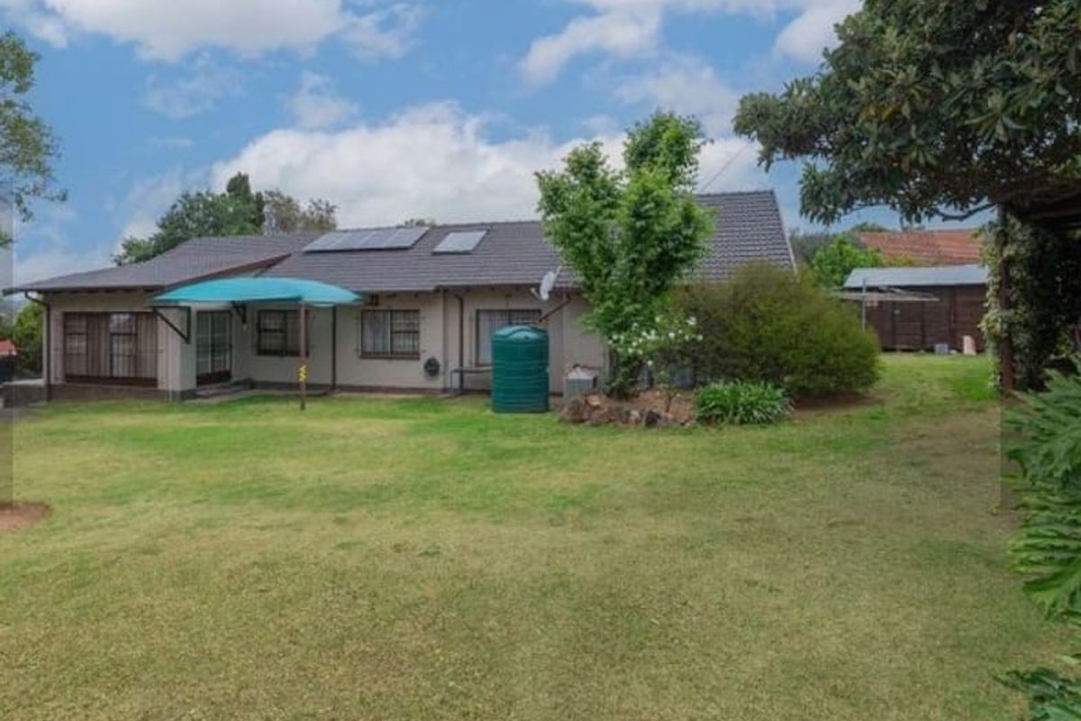 Rear view of the house featuring a tiled roof with solar panels, a spacious lawn, and a water storage tank.