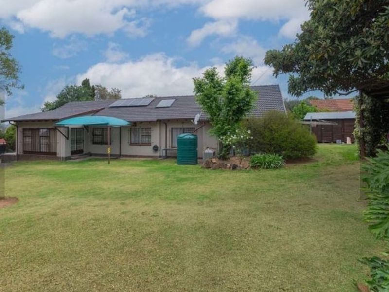 Rear view of the house featuring a tiled roof with solar panels, a spacious lawn, and a water storage tank.