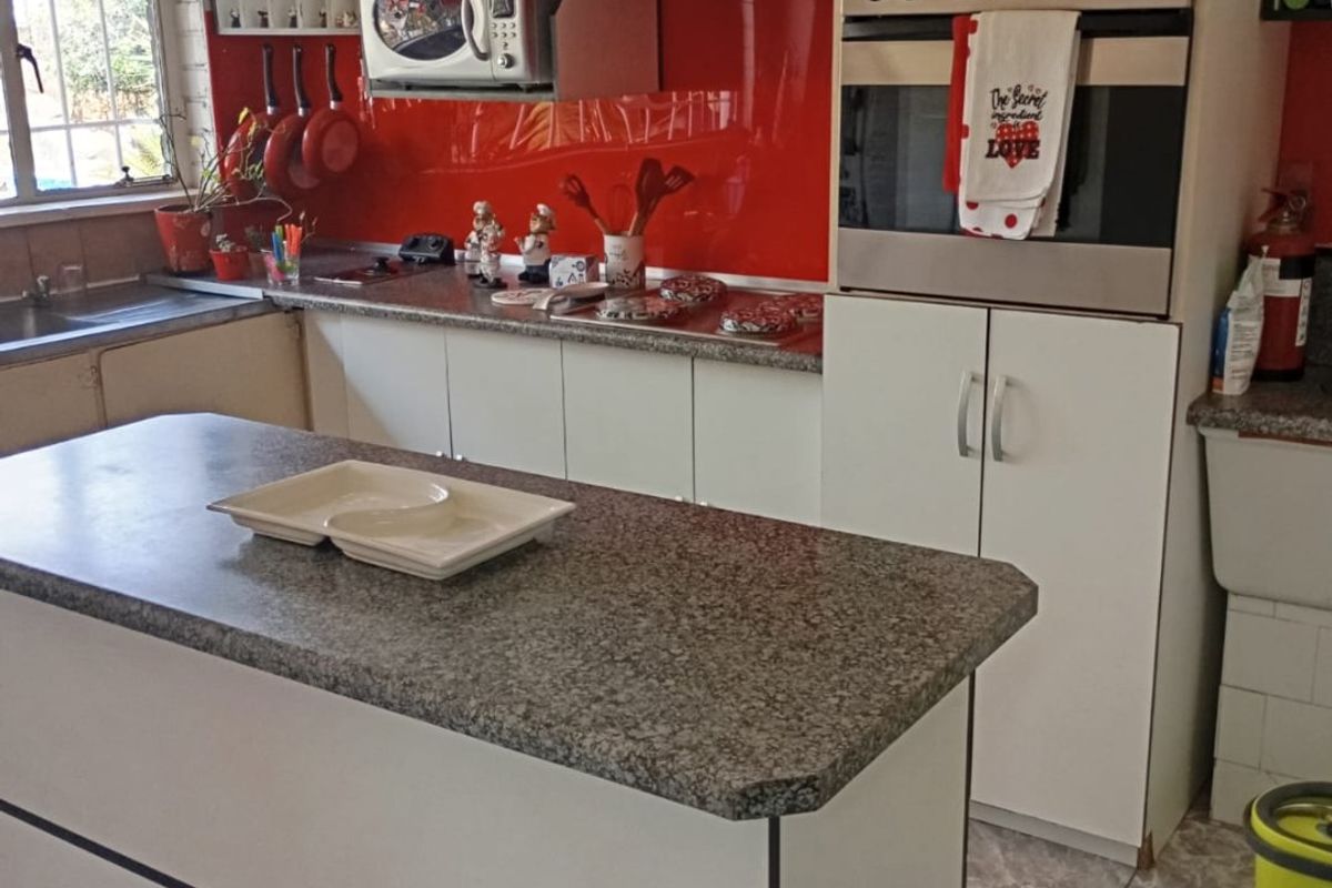 A functional kitchen featuring a central island, granite countertops, built-in oven, and a vibrant red glass backsplash with ample storage cabinetry.