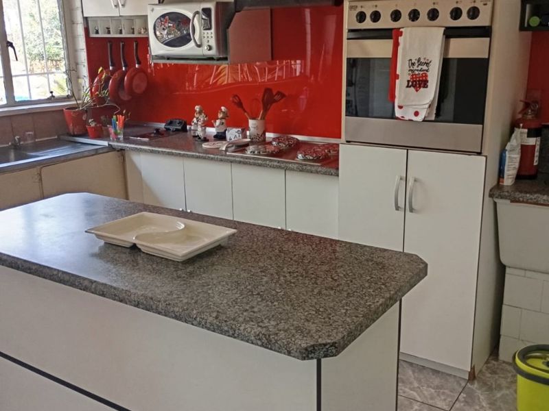 A functional kitchen featuring a central island, granite countertops, built-in oven, and a vibrant red glass backsplash with ample storage cabinetry.