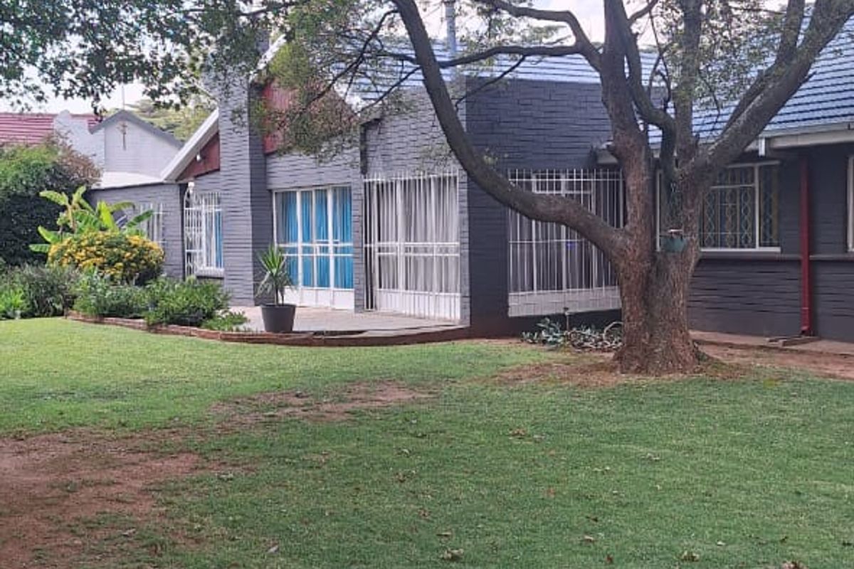 Rear view of the property featuring a dark-painted brick facade, tiled roof, security bars on windows, and a paved patio area overlooking a garden.