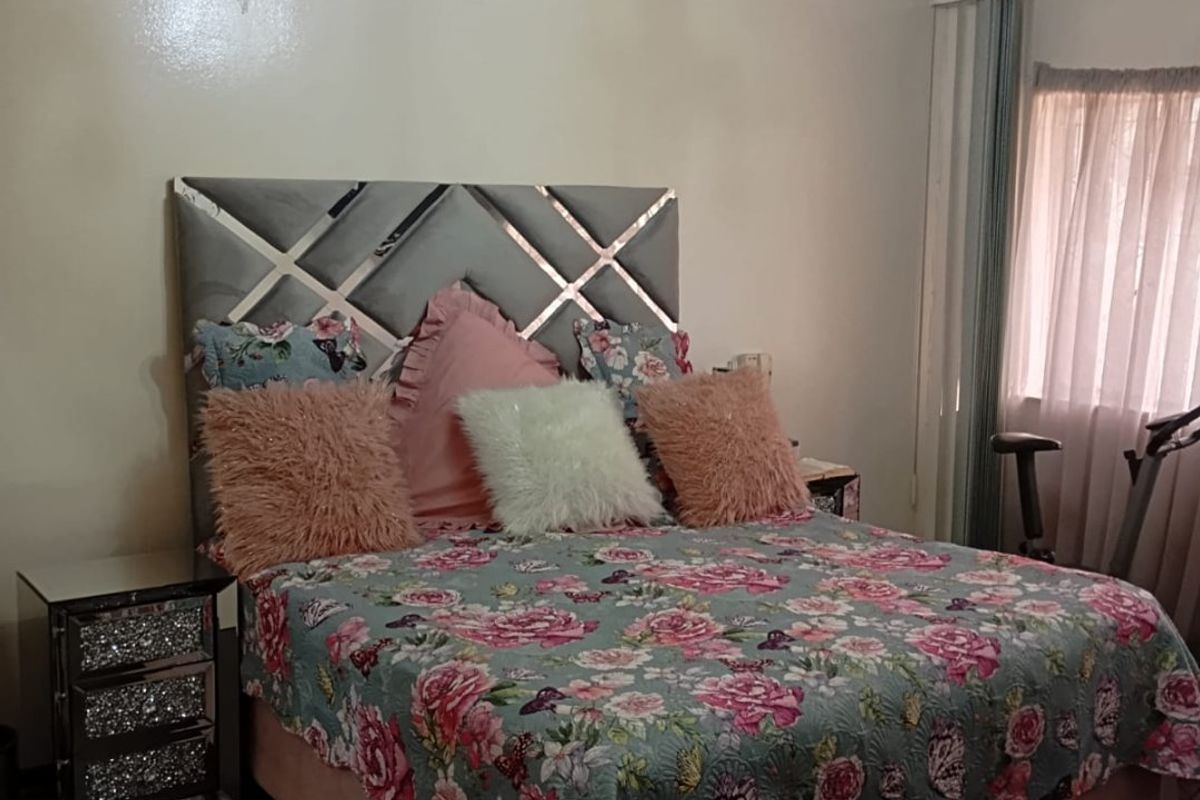 A standard bedroom featuring a central ceiling chandelier and window curtain tracks, with visible signs of wear on the ceiling plaster.