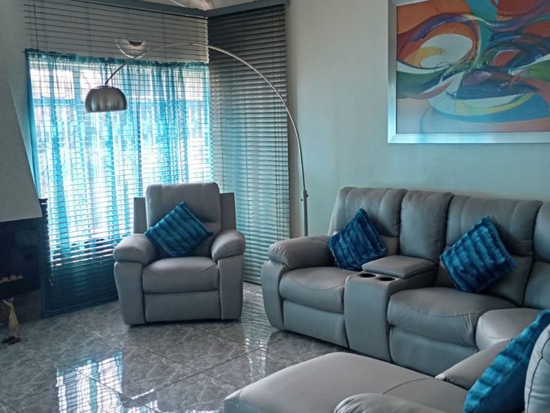 A comfortable living room featuring polished tiled flooring, a built-in fireplace, and large windows fitted with venetian blinds.