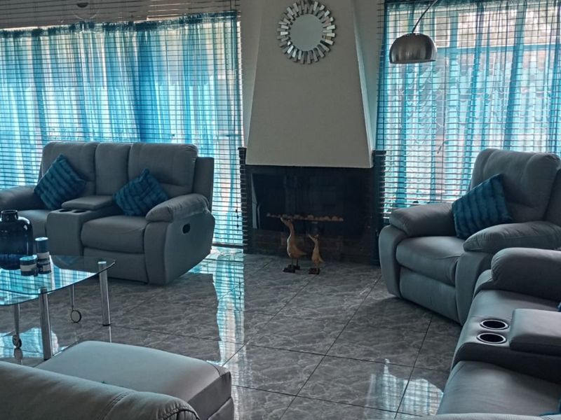Spacious living room featuring a central fireplace, polished tiled flooring, and large windows fitted with venetian blinds.