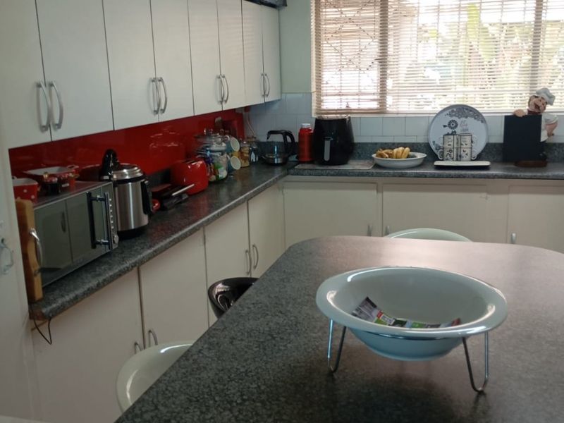 A functional kitchen featuring white cabinetry, grey laminate countertops, and a vibrant red glass splashback, providing ample storage and workspace.