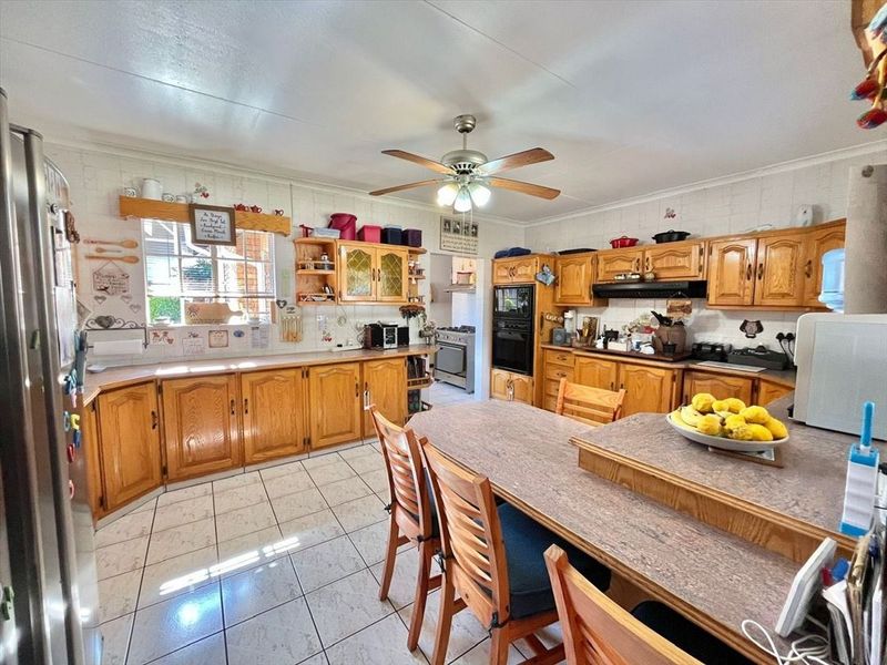 A spacious kitchen featuring traditional wooden cabinetry, built-in oven, extractor fan, and tiled flooring, offering a functional layout with ample storage space.