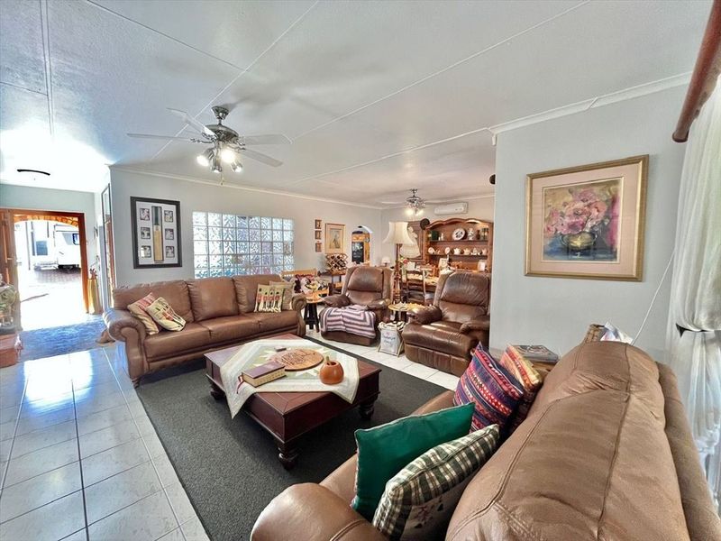 Spacious open-plan living and dining area featuring tiled flooring, ceiling fans, and a distinctive glass block window providing natural light.