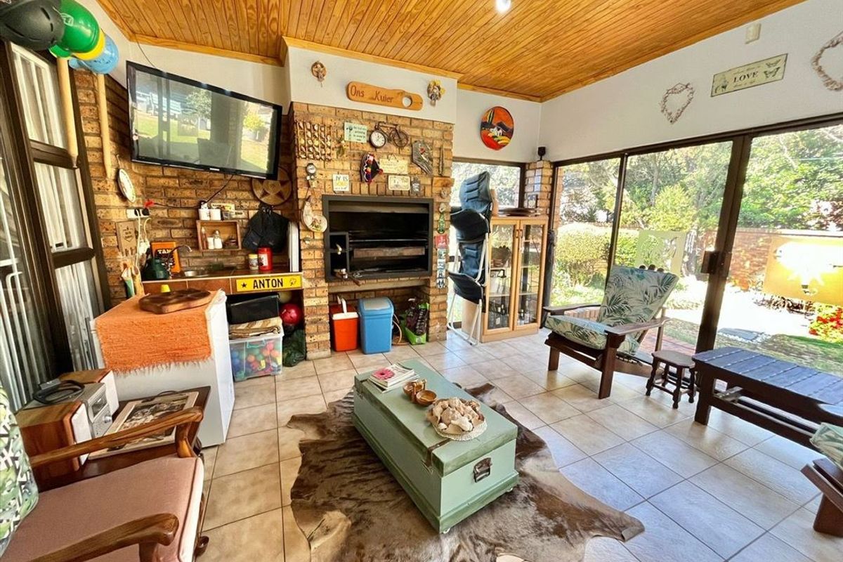 Enclosed patio area featuring a built-in braai, timber ceiling, and tiled flooring with direct access to the garden through sliding glass doors.