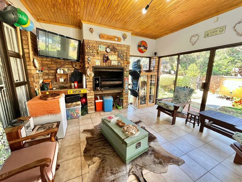 Enclosed patio area featuring a built-in braai, timber ceiling, and tiled flooring with direct access to the garden through sliding glass doors.