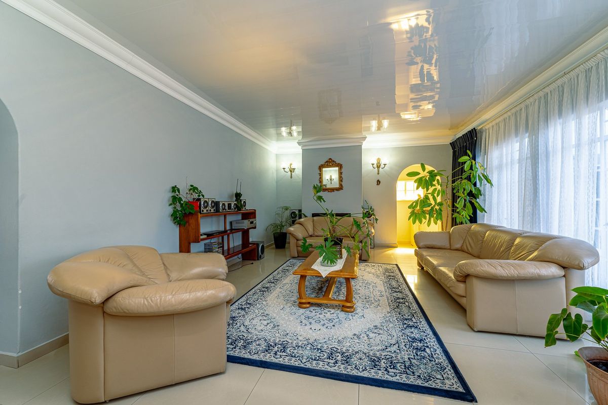 Spacious living room featuring a high-gloss reflective ceiling, crown molding, and neutral tiled flooring, leading through an archway to adjacent living areas.