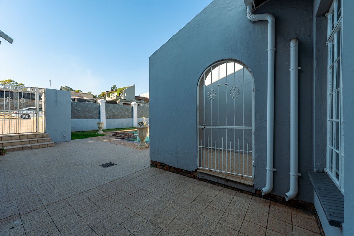 Rear exterior view featuring a tiled patio area, a secure wrought iron gate, and access to the swimming pool and boundary wall.