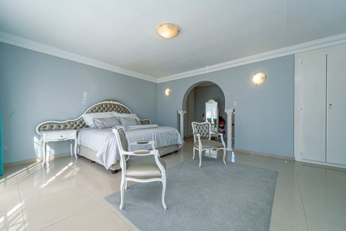 Spacious bedroom featuring light blue walls, tiled flooring, coved cornicing, and a decorative arched entryway leading to an adjoining space.