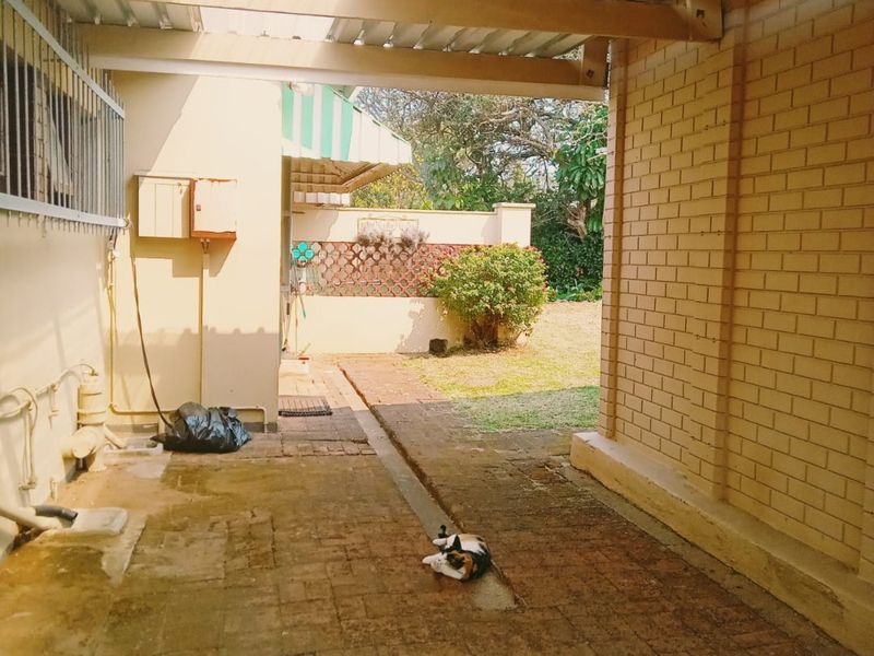 A covered outdoor patio area featuring brick paving and exposed brick walls, providing a functional space leading out to the garden.