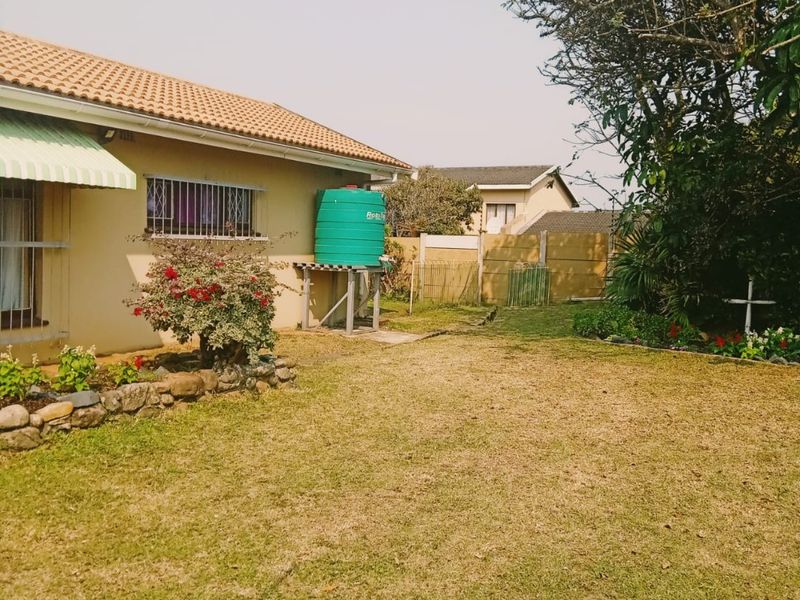 Rear exterior view of the property featuring a lawn, water storage tank, and perimeter precast concrete walling.