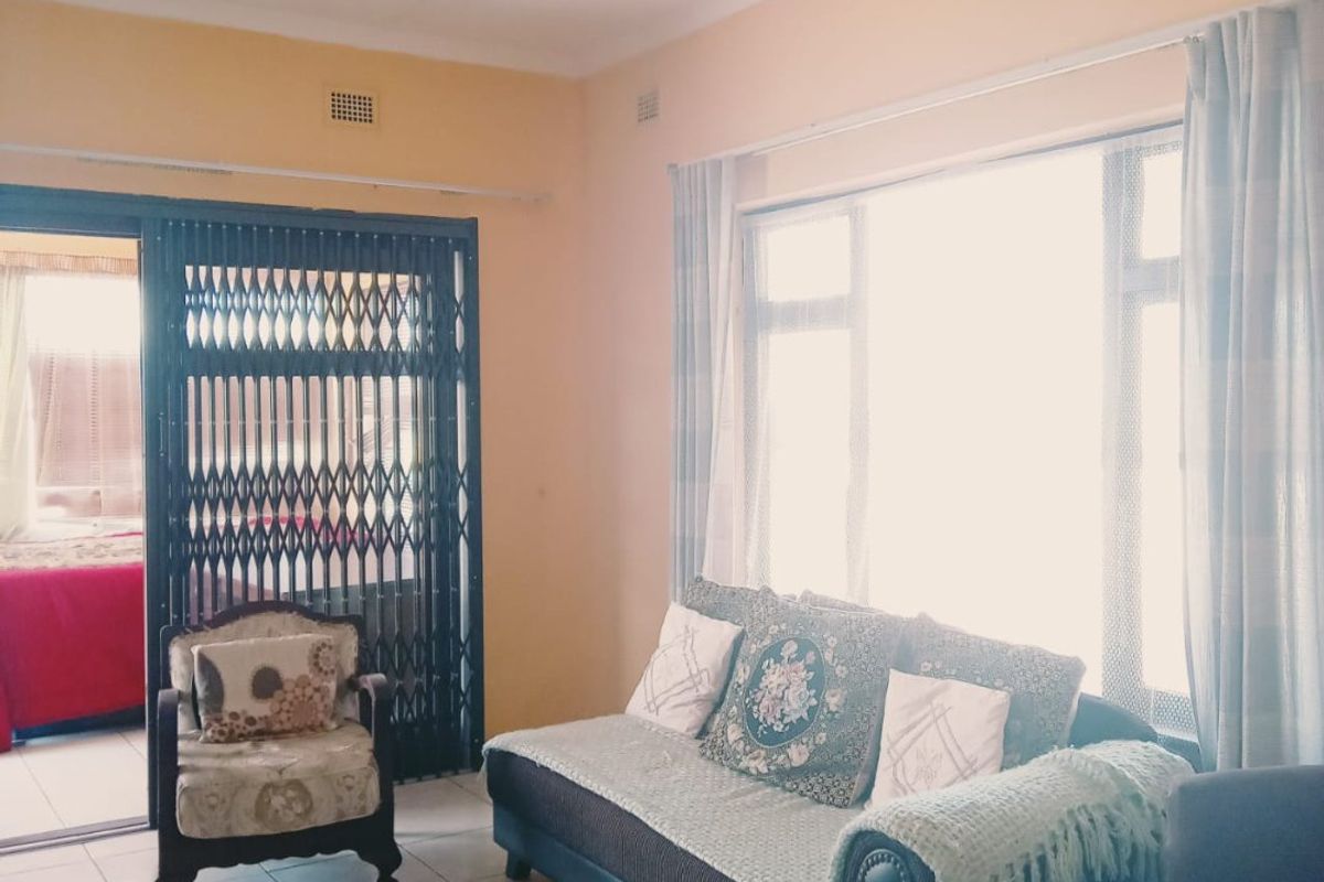 A living room featuring tiled flooring, a large window for natural light, and a sliding security gate leading to an adjacent space.