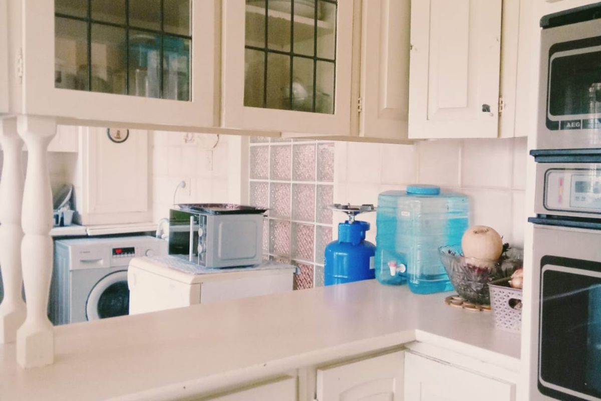 A dated kitchen featuring built-in cabinetry, glass-fronted upper cupboards, and a built-in oven, with a view through to an adjacent laundry area.
