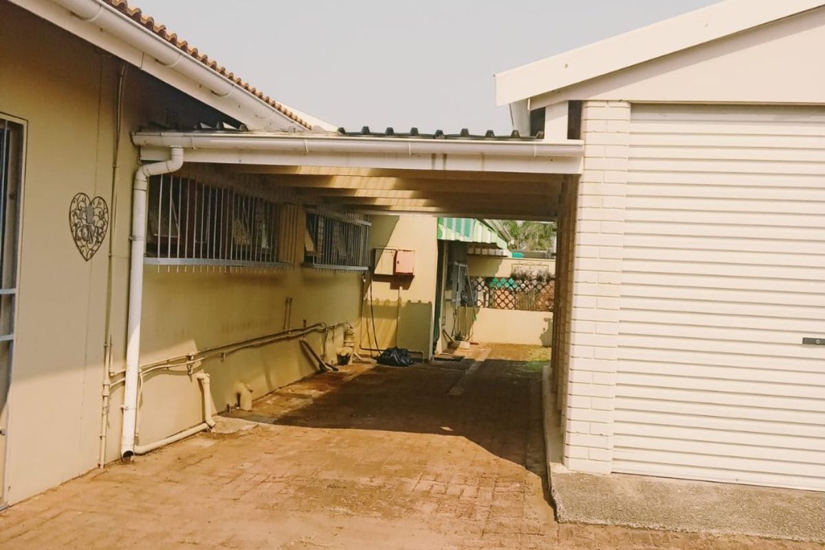 A covered carport area connecting the main house to the garage, featuring brick paving and functional guttering systems.