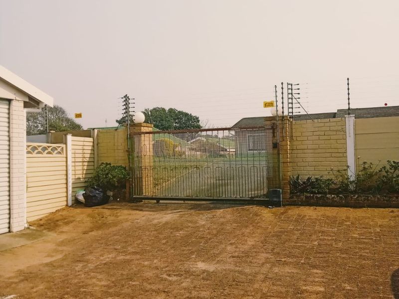 Front exterior view featuring a paved driveway, sliding gate with electric fencing, and a brick boundary wall.