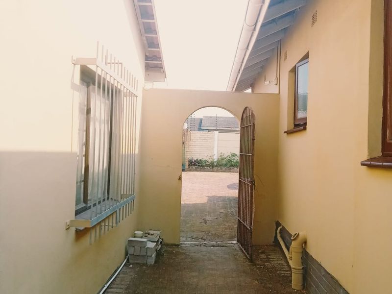 A narrow paved side passage between two building sections, featuring an arched gateway leading to the rear courtyard area.