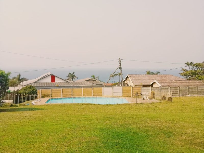A spacious backyard featuring a swimming pool, well-maintained lawn, and perimeter fencing with a distant ocean view.
