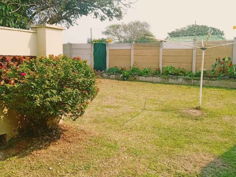 A private backyard featuring a lawn, established shrubbery, and secure perimeter walling with electric fencing.