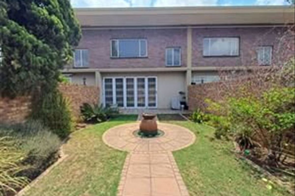 Rear view of the townhouse featuring a brick facade, paved garden walkway, and sliding glass doors leading to the interior living space.