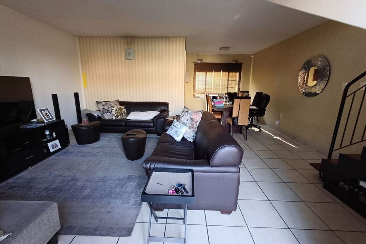 Spacious open-plan living and dining area featuring tiled flooring, neutral wall finishes, and a staircase leading to the upper level.