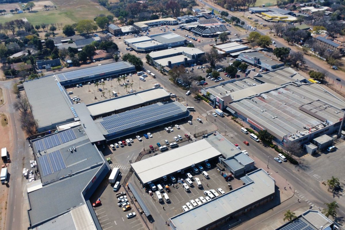 Aerial view of a commercial shopping center complex featuring multiple buildings, extensive parking facilities, and rooftop solar panel installations.