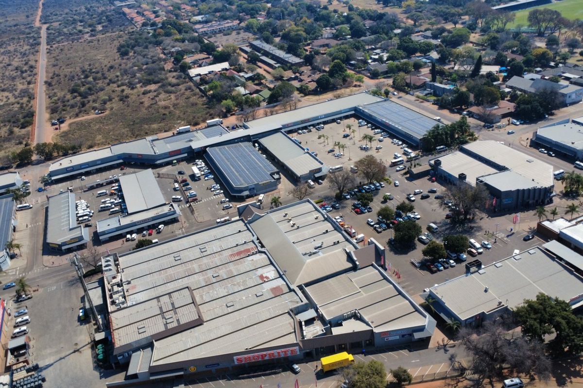 Aerial view of a commercial shopping center complex featuring extensive parking facilities and multiple retail buildings with solar panel installations.
