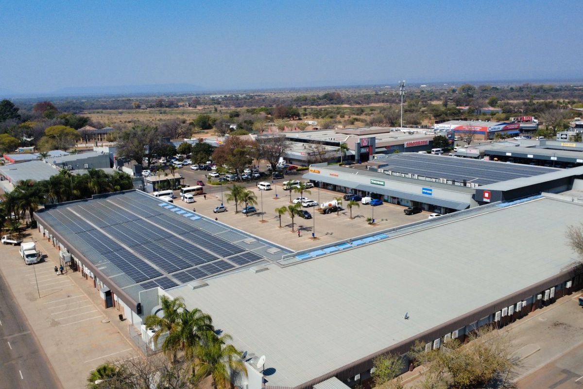 Aerial view of a commercial shopping center complex featuring extensive rooftop solar panel installations and a central paved parking area.