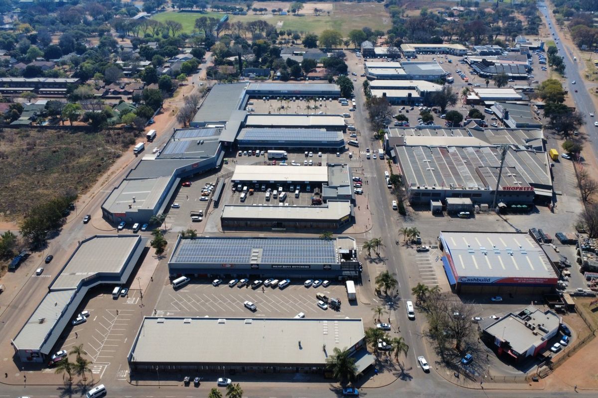 Aerial view of a commercial shopping center complex featuring multiple retail buildings, extensive parking facilities, and solar panel installations on rooftops.