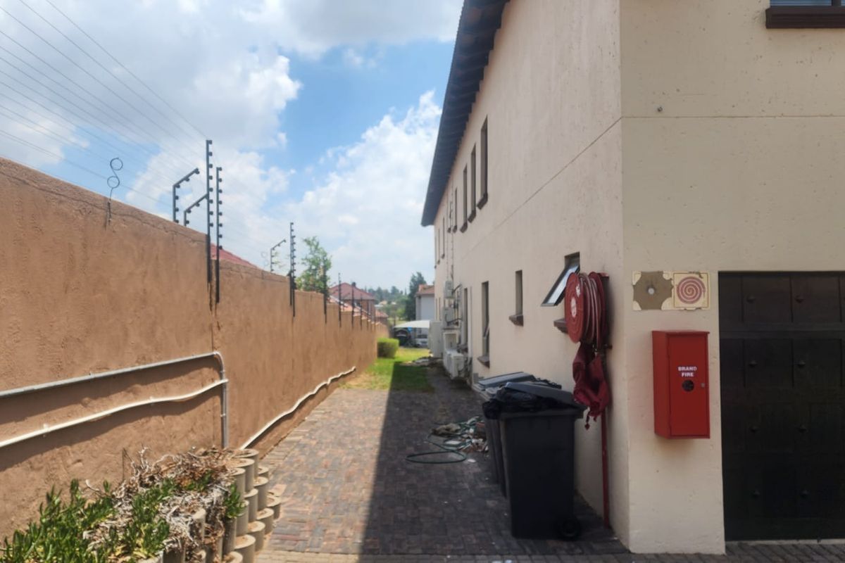 Side exterior passage of a commercial building featuring paved flooring, electric security fencing, and mounted fire safety equipment.