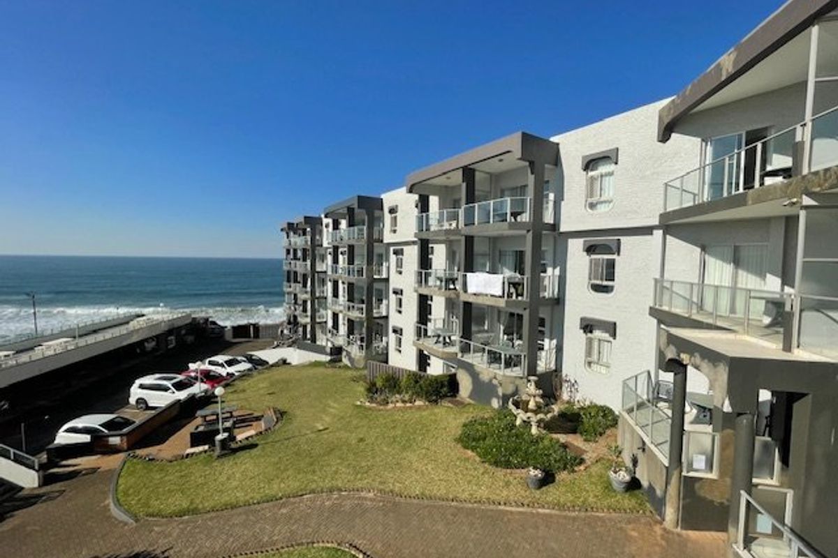 Exterior view of an apartment complex featuring private balconies with glass balustrades, overlooking a landscaped garden area and the ocean.