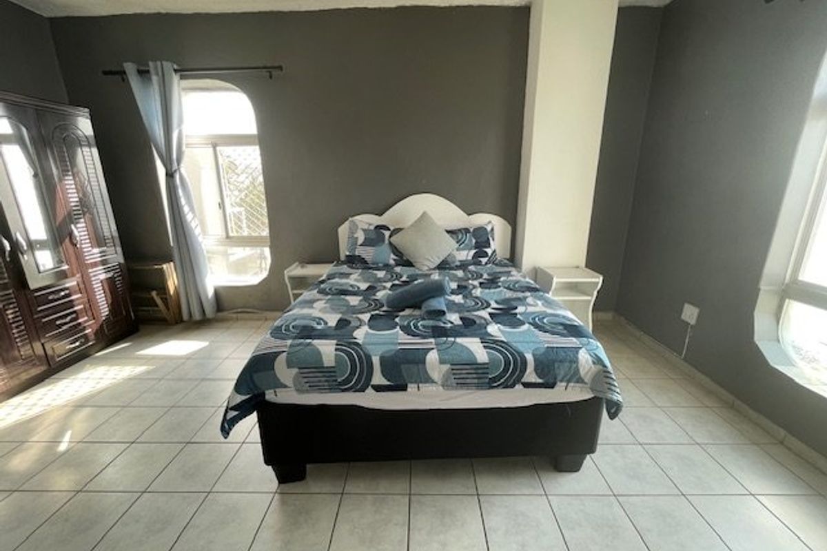 A bedroom featuring tiled flooring, an arched window, and a ceiling fan, with dark grey walls and a central structural pillar.
