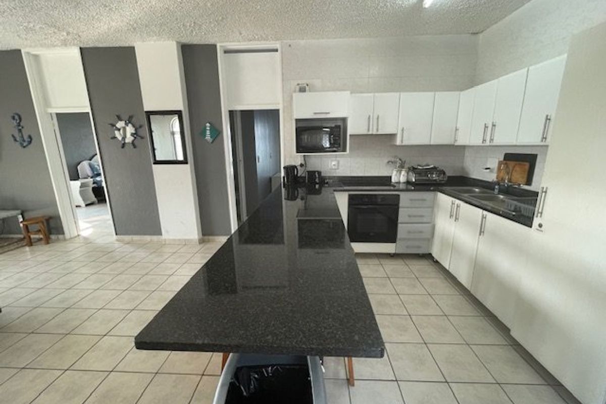A functional kitchen featuring a long granite breakfast bar, built-in oven, microwave, and ample white cabinetry with tiled flooring throughout.