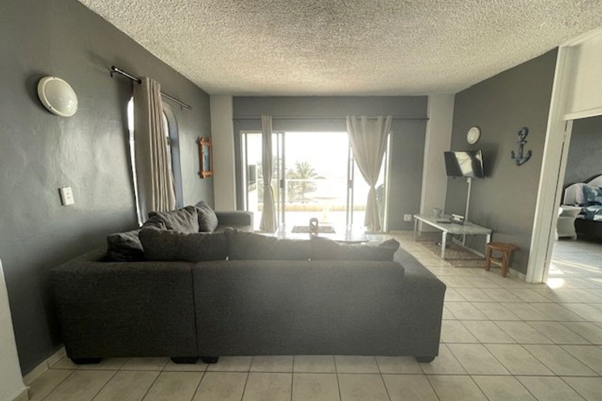 A spacious living room featuring tiled flooring, textured ceilings, and large sliding glass doors that provide natural light and access to the balcony.
