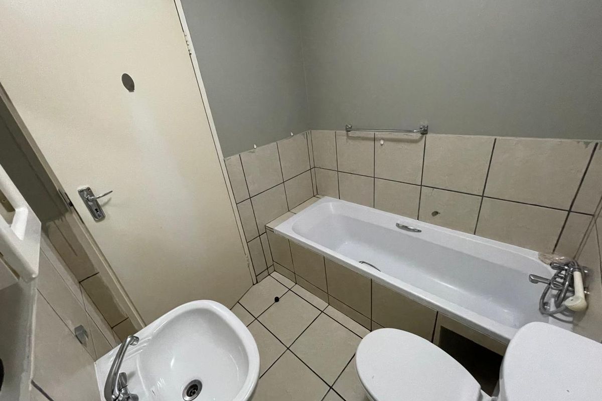 A functional bathroom featuring a bathtub, pedestal sink, and toilet, with tiled walls and flooring. The space requires cosmetic updates and maintenance.
