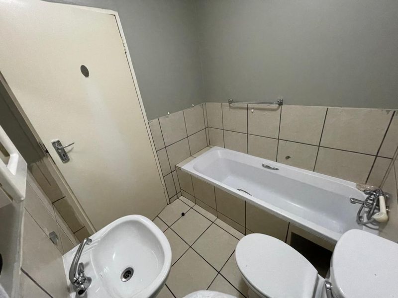 A functional bathroom featuring a bathtub, pedestal sink, and toilet, with tiled walls and flooring. The space requires cosmetic updates and maintenance.