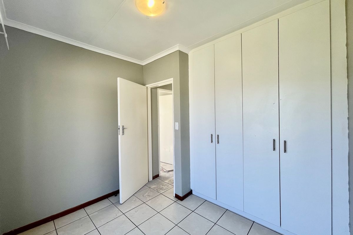 A vacant bedroom featuring neutral wall paint, tiled flooring, and ample built-in cupboard storage space.
