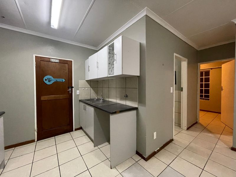 A functional scullery area featuring built-in cabinetry, a stainless steel sink, tiled backsplash, and tiled flooring, providing a practical utility space.