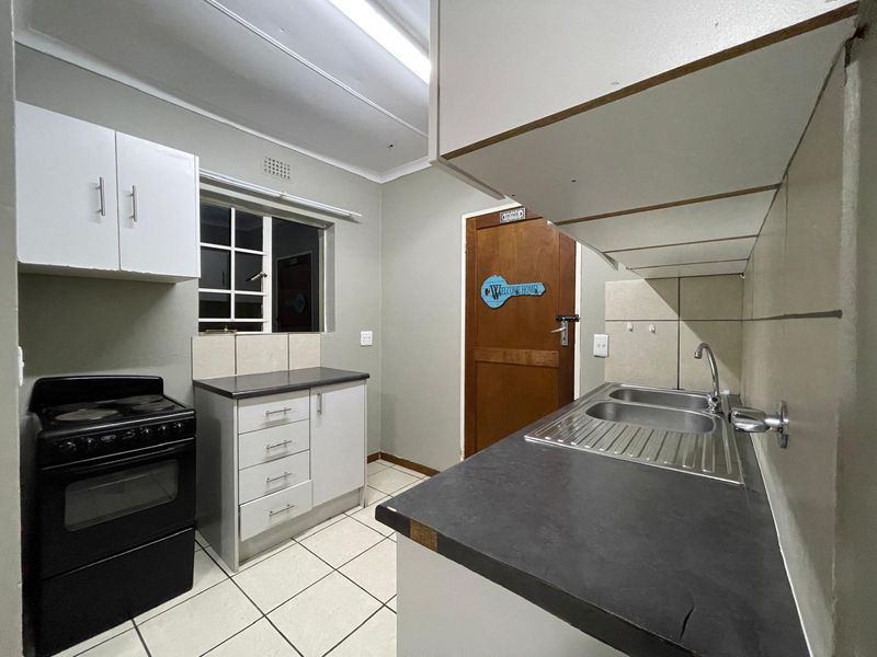 A functional kitchen featuring built-in cabinetry, laminate countertops, a stainless steel double sink, and tiled flooring.