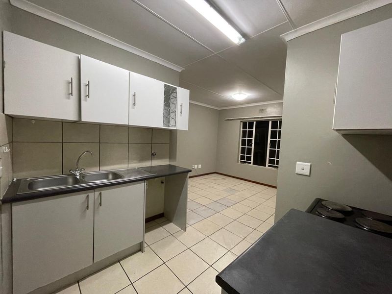 An open-plan kitchen and living area featuring tiled flooring, built-in cabinetry, and an electric stove, offering a functional space ready for updates.