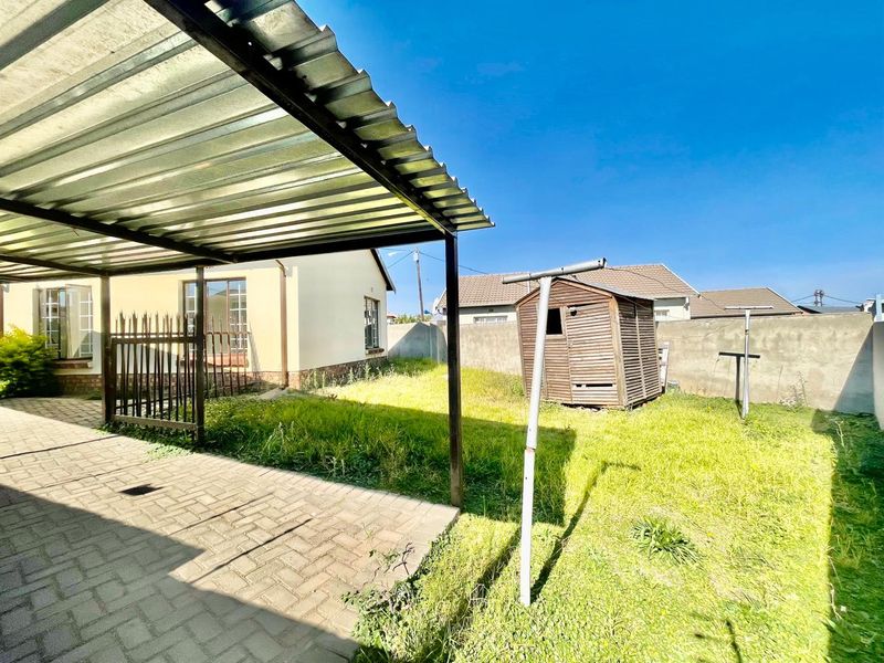 Rear garden area featuring a paved patio with a corrugated metal roof, perimeter boundary walls, and a small wooden storage shed.