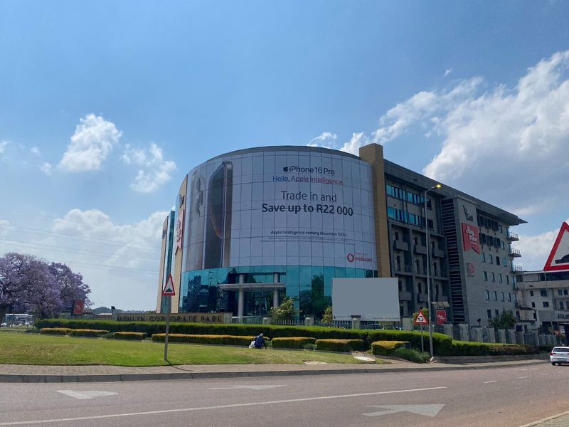 A view of the Menlyn Corporate Park commercial building featuring a prominent glass facade and large-scale advertising signage.