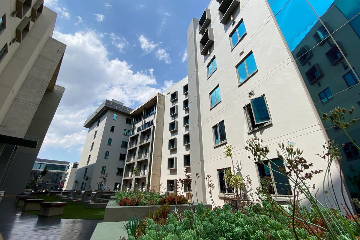 A modern multi-story commercial building exterior featuring reflective glass windows, structured facade design, and landscaped outdoor areas with decking.