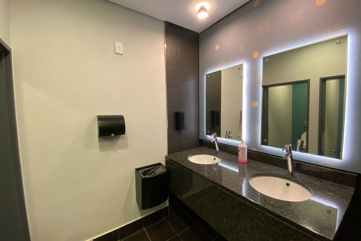 Modern commercial bathroom featuring a double vanity with granite countertops, undermount sinks, and stylish backlit mirrors.